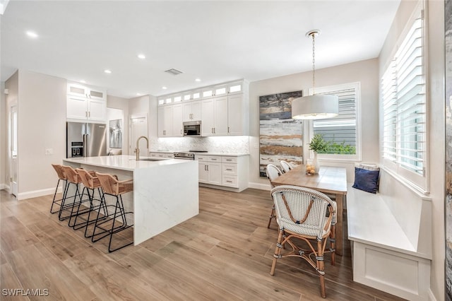 kitchen with white cabinets, sink, decorative light fixtures, appliances with stainless steel finishes, and light wood-type flooring