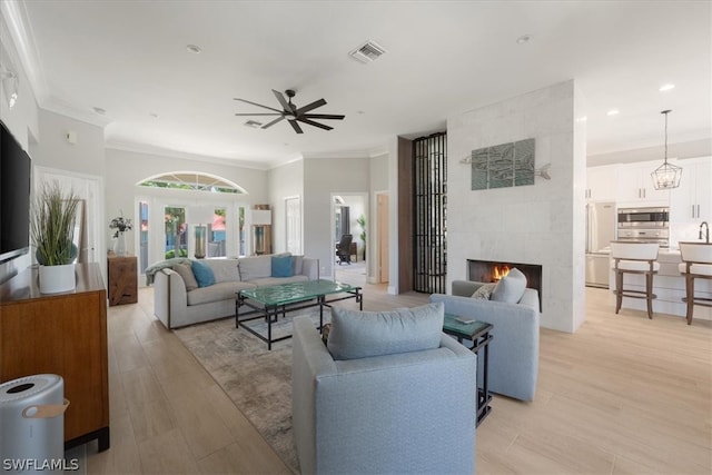 living room with crown molding, ceiling fan, a tiled fireplace, and light hardwood / wood-style floors