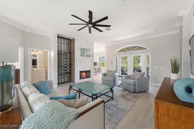 living room featuring a fireplace, ornamental molding, ceiling fan, light wood-type flooring, and french doors