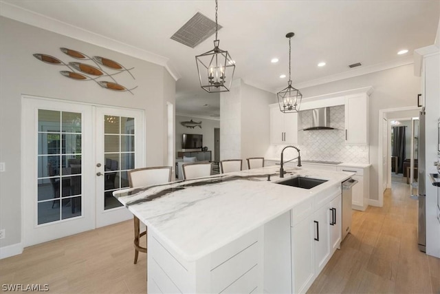 kitchen featuring white cabinetry, wall chimney exhaust hood, a kitchen island with sink, and a breakfast bar area