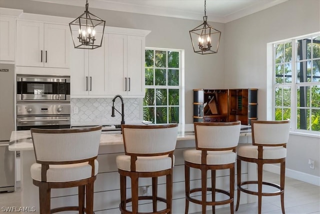 kitchen with pendant lighting, appliances with stainless steel finishes, white cabinetry, backsplash, and a kitchen island