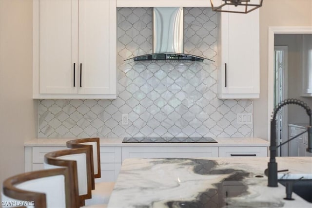 kitchen featuring backsplash, white cabinets, light stone countertops, black electric cooktop, and wall chimney exhaust hood