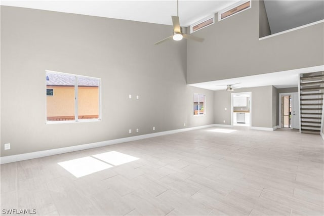 unfurnished living room featuring ceiling fan and a towering ceiling