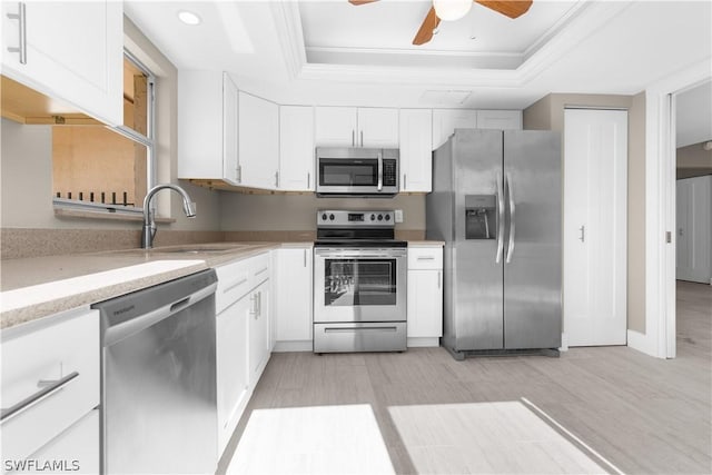 kitchen featuring stainless steel appliances, a raised ceiling, white cabinets, and crown molding