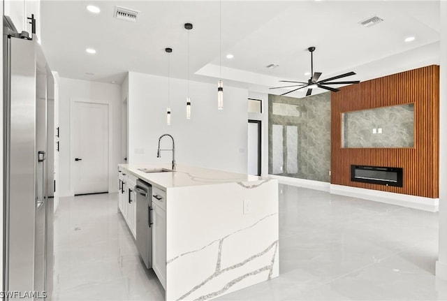 kitchen featuring decorative light fixtures, white cabinetry, sink, a kitchen island with sink, and light stone counters