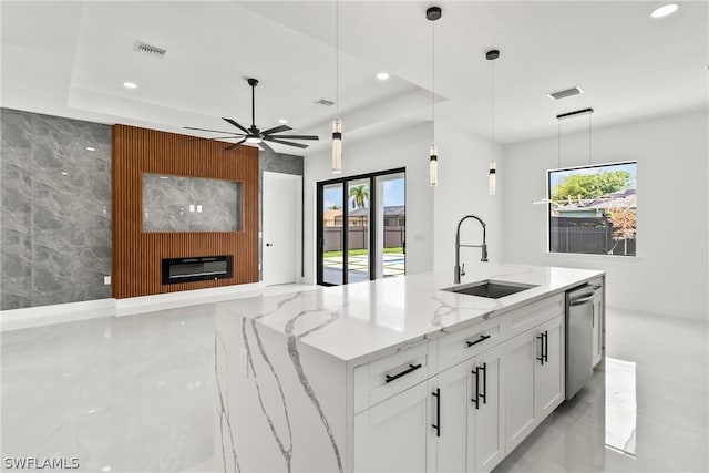 kitchen featuring dishwasher, sink, white cabinets, light stone counters, and a center island with sink