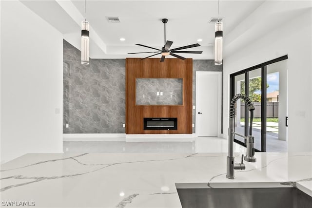 kitchen featuring pendant lighting, sink, ceiling fan, light stone counters, and a fireplace