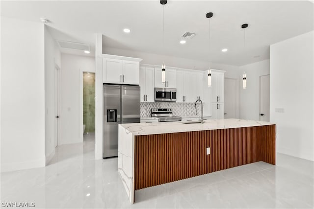 kitchen featuring appliances with stainless steel finishes, decorative light fixtures, sink, white cabinets, and a center island with sink