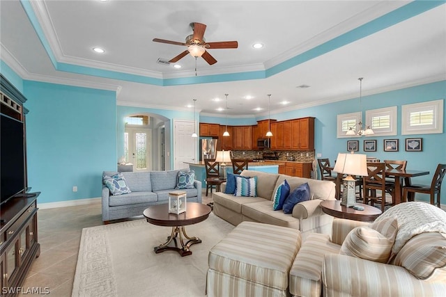 tiled living room with ceiling fan with notable chandelier, ornamental molding, and a raised ceiling