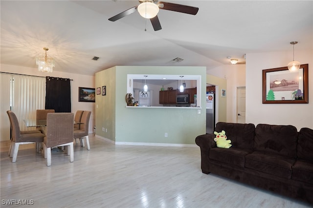 living room featuring ceiling fan with notable chandelier, light wood-type flooring, and vaulted ceiling