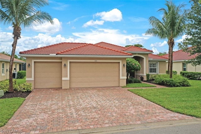 mediterranean / spanish-style house with decorative driveway, stucco siding, an attached garage, a front yard, and a tiled roof