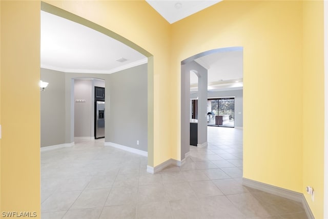 hallway featuring light tile patterned floors, baseboards, arched walkways, and crown molding