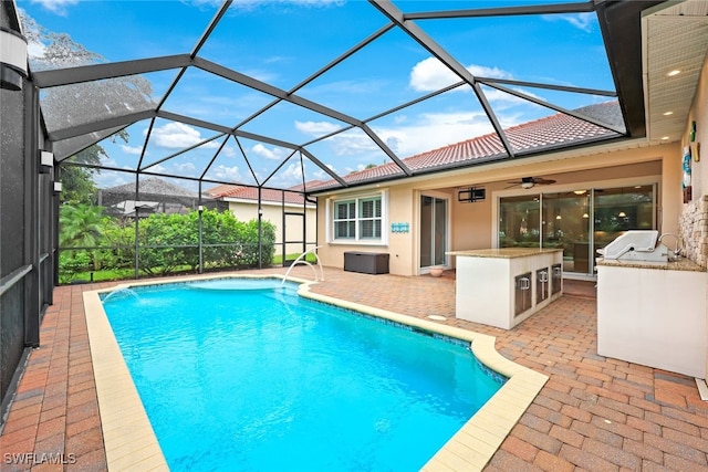 outdoor pool featuring a patio, area for grilling, glass enclosure, ceiling fan, and an outdoor bar