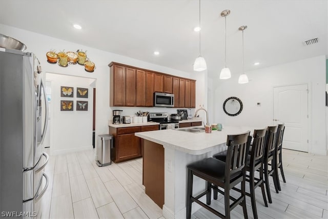 kitchen featuring stainless steel appliances, pendant lighting, sink, a breakfast bar, and a kitchen island with sink