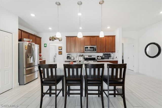 kitchen featuring hanging light fixtures, appliances with stainless steel finishes, a center island with sink, and a breakfast bar