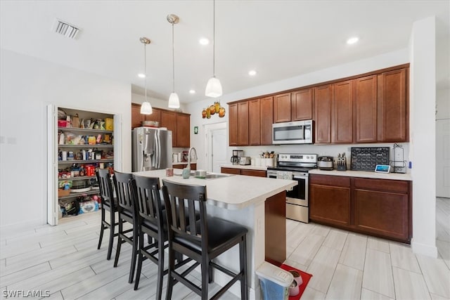 kitchen featuring stainless steel appliances, sink, hanging light fixtures, a kitchen breakfast bar, and an island with sink