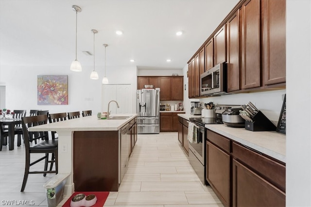 kitchen with a breakfast bar, an island with sink, appliances with stainless steel finishes, pendant lighting, and sink