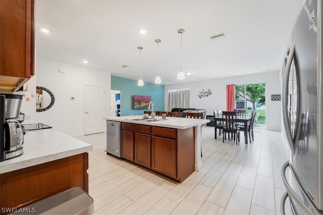 kitchen featuring sink, appliances with stainless steel finishes, decorative light fixtures, and an island with sink