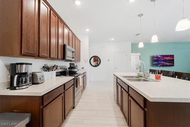 kitchen with stainless steel appliances, decorative light fixtures, sink, and an island with sink