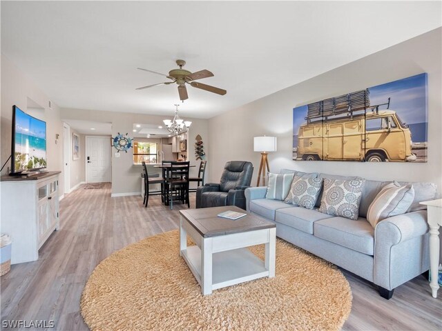 living room featuring ceiling fan with notable chandelier and light wood-type flooring