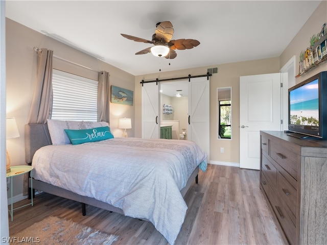 bedroom with ensuite bathroom, a barn door, ceiling fan, and hardwood / wood-style floors