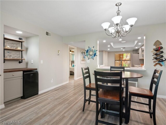 dining space featuring light hardwood / wood-style floors, a raised ceiling, and a notable chandelier