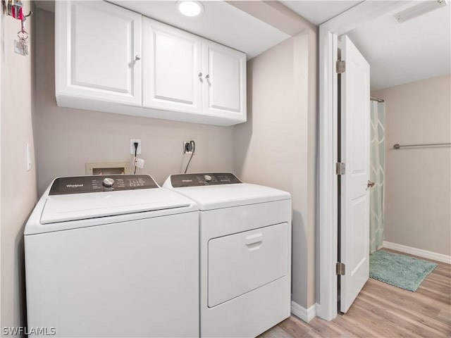 laundry area with washing machine and clothes dryer, light hardwood / wood-style flooring, and cabinets