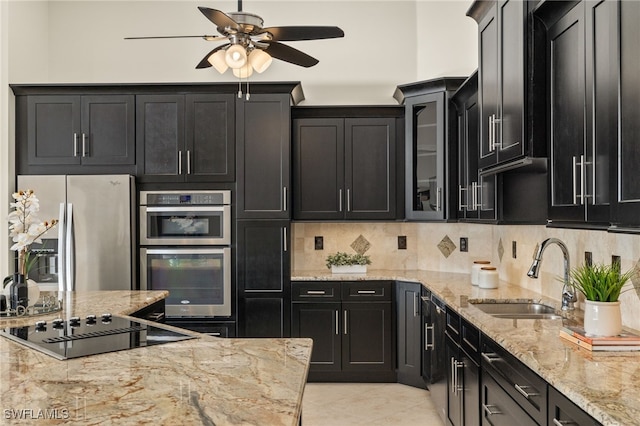 kitchen featuring sink, backsplash, ceiling fan, stainless steel appliances, and light stone countertops