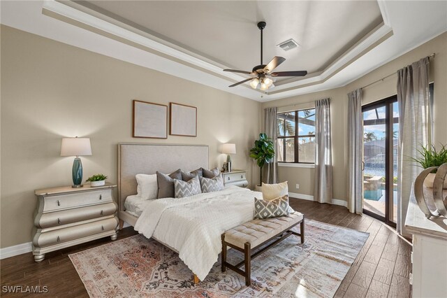 bedroom with dark wood-type flooring, ceiling fan, a tray ceiling, and access to exterior