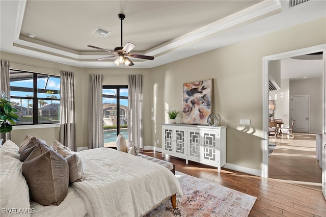 bedroom featuring a raised ceiling, crown molding, hardwood / wood-style floors, and access to exterior