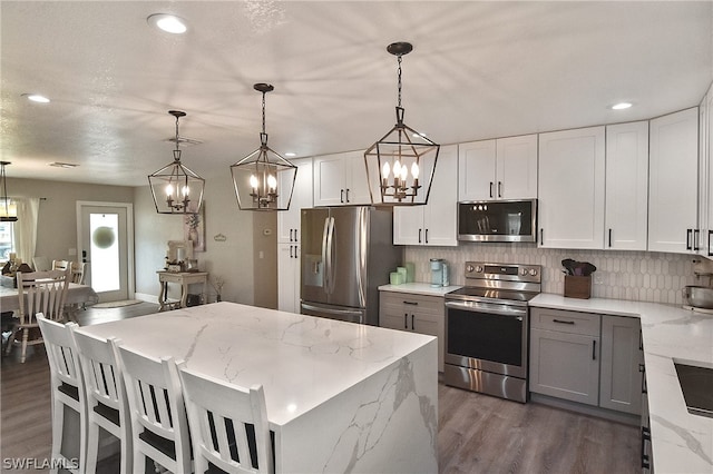 kitchen with backsplash, dark hardwood / wood-style floors, stainless steel appliances, light stone countertops, and decorative light fixtures