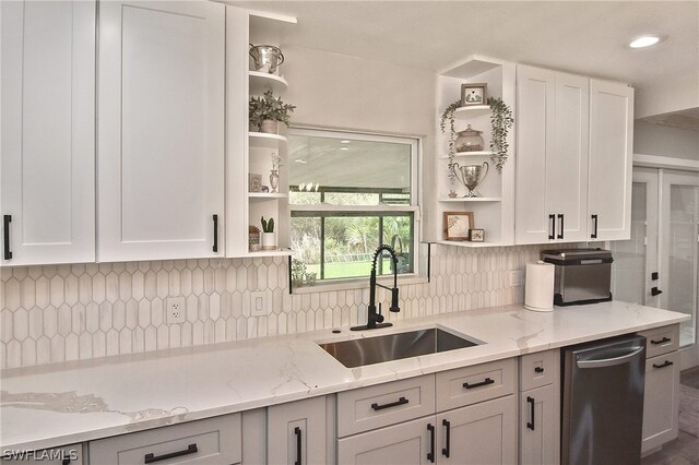 kitchen featuring white cabinets, sink, light stone counters, stainless steel dishwasher, and decorative backsplash