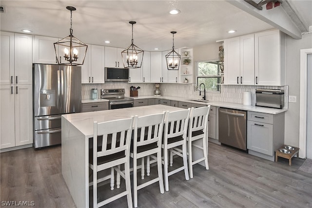 kitchen with decorative backsplash, appliances with stainless steel finishes, pendant lighting, and wood-type flooring