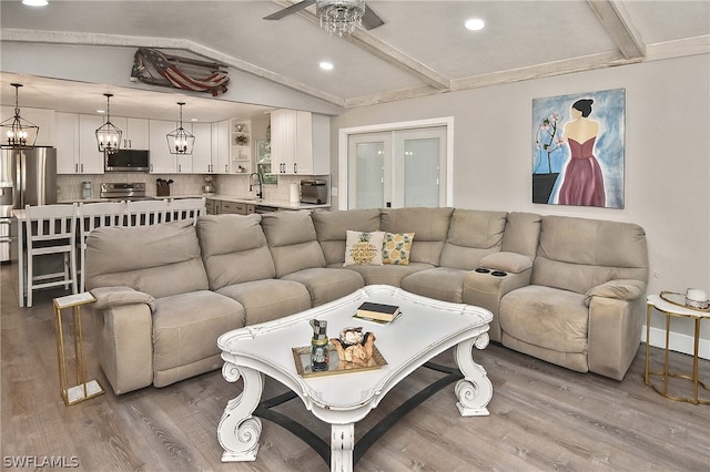 living room with sink, vaulted ceiling with beams, ceiling fan with notable chandelier, and hardwood / wood-style floors