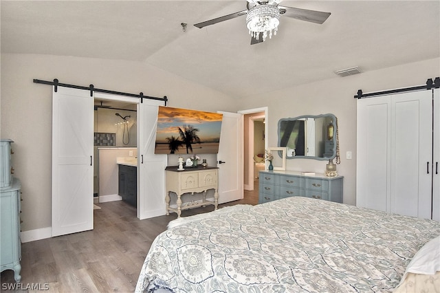 bedroom featuring hardwood / wood-style flooring, ceiling fan, ensuite bath, a barn door, and vaulted ceiling