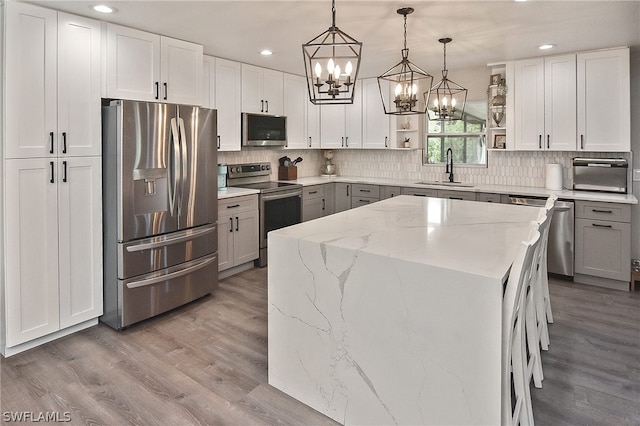 kitchen with tasteful backsplash, stainless steel appliances, hanging light fixtures, sink, and light hardwood / wood-style flooring