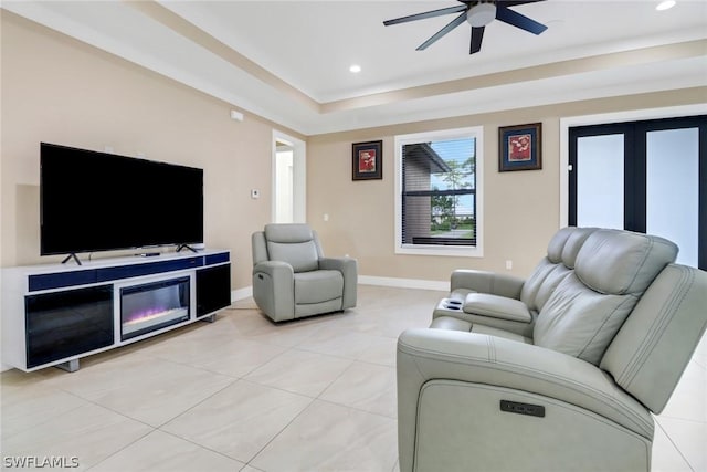 tiled living room featuring ceiling fan and a tray ceiling