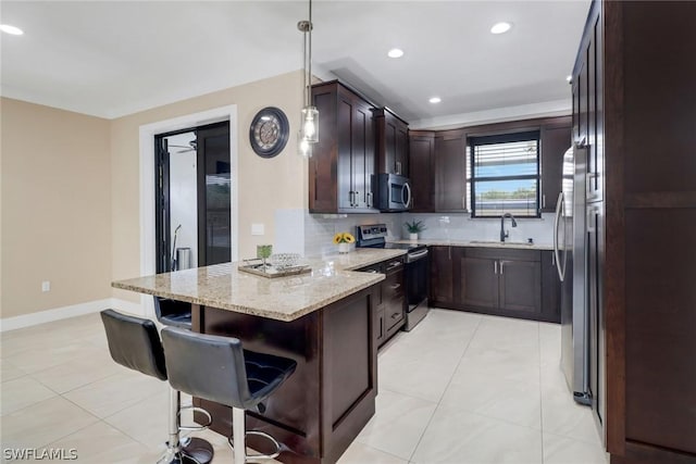 kitchen featuring sink, a breakfast bar area, stainless steel appliances, light stone counters, and decorative light fixtures