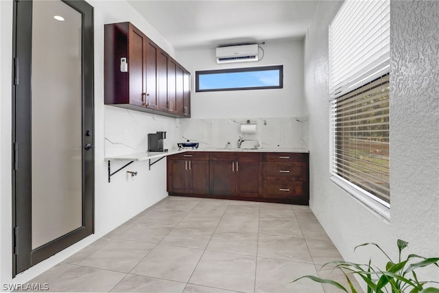 kitchen featuring sink, light tile patterned floors, tasteful backsplash, light stone countertops, and an AC wall unit