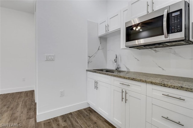 kitchen with dark wood-type flooring, sink, light stone counters, decorative backsplash, and white cabinets