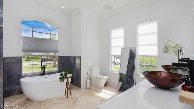 bathroom featuring toilet, ornamental molding, a bath, and plenty of natural light