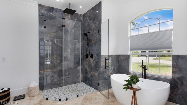 bathroom with a stall shower, a freestanding tub, plenty of natural light, and tile walls