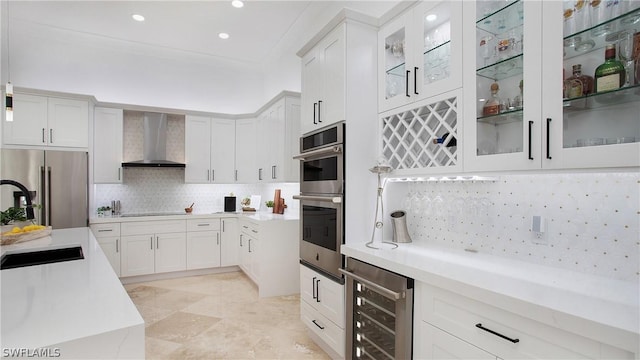 kitchen featuring wall chimney exhaust hood, wine cooler, glass insert cabinets, light countertops, and stainless steel appliances