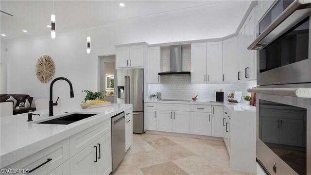 kitchen featuring appliances with stainless steel finishes, hanging light fixtures, white cabinets, wall chimney range hood, and sink