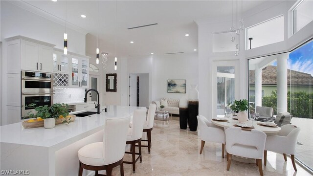 kitchen featuring decorative light fixtures, backsplash, double oven, white cabinets, and sink