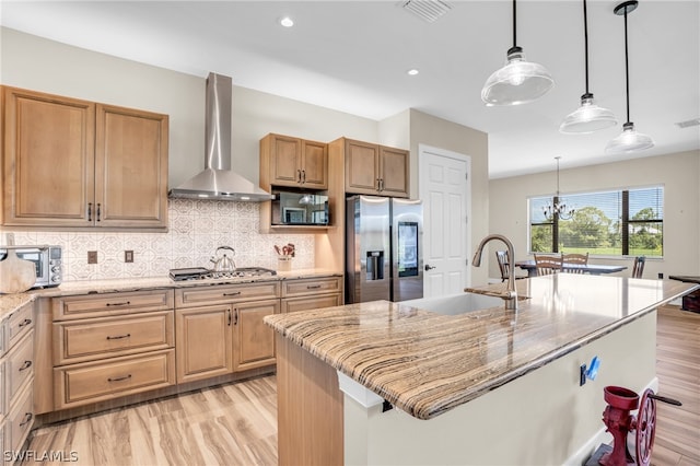 kitchen with wall chimney range hood, stainless steel appliances, sink, and an island with sink