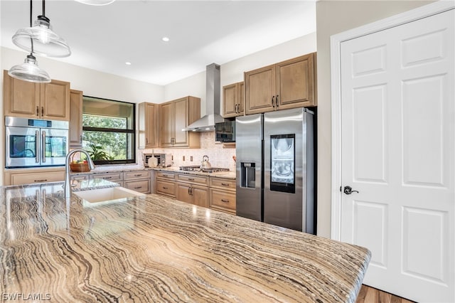 kitchen with wall chimney range hood, stainless steel appliances, sink, light stone counters, and tasteful backsplash