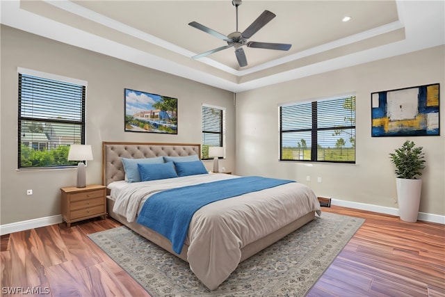 bedroom with ceiling fan, multiple windows, wood-type flooring, and a raised ceiling