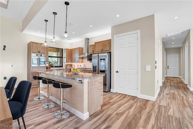 kitchen featuring wall chimney range hood, hanging light fixtures, a kitchen island, a breakfast bar, and stainless steel appliances