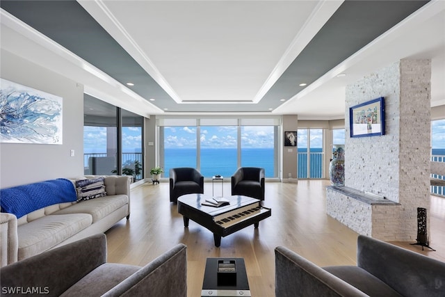 living room featuring light hardwood / wood-style floors, a raised ceiling, ornamental molding, a water view, and a wall of windows